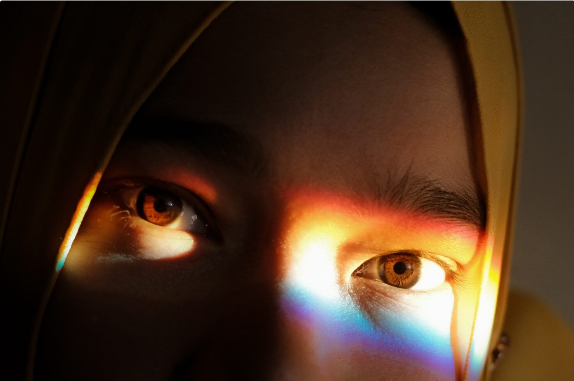 Close-up de um olho iluminado por um feixe de luz prismática, remetendo à visão e à percepção de cores